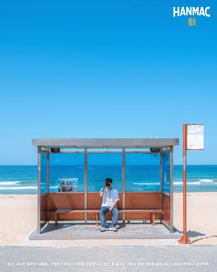한맥 장소 디스커버리 세번째 에피소드 부드러운 바다와 파도 명소 세번째 강릉 주문진해수욕장 끄트머리에 위차한 BTS 버스정류장에서 남성이 카메라를 들고 있습니다.