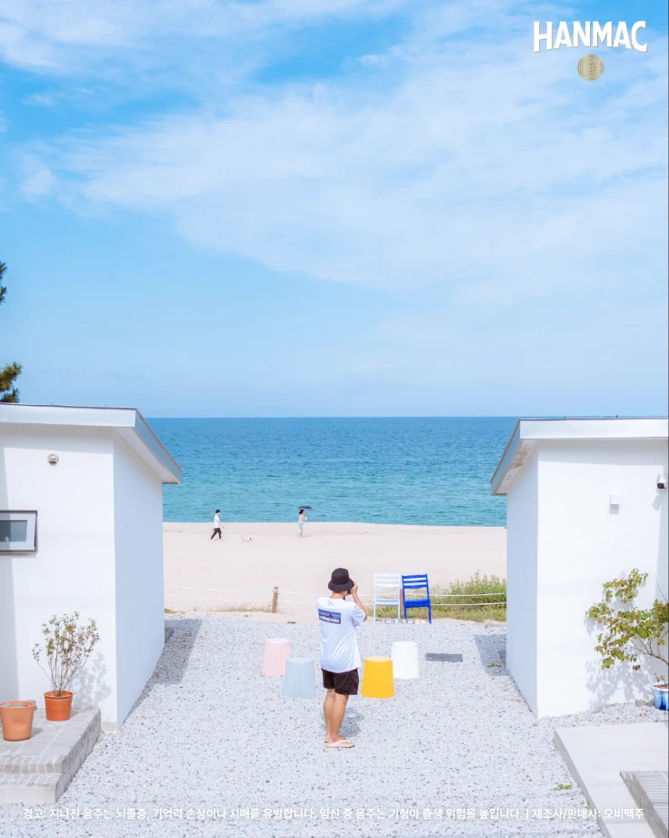 한맥 장소 디스커버리 세번째 에피소드 부드러운 바다와 파도 명소 첫,두번째 사근진 해변에서 하얀 집들 사이에서 남성이 카메라로 바다를 찍고 있습니다.
