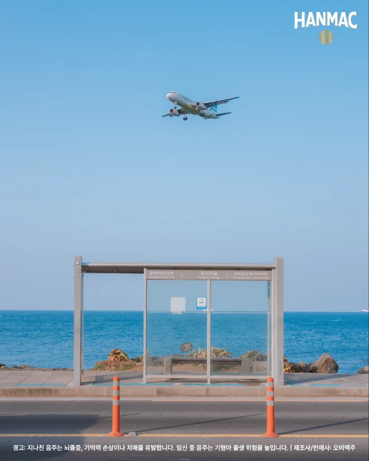 한맥 장소 디스커버리 세번째 에피소드 부드러운 바다와 파도 명소 일곱번째 제주 용마마을 버스정류장의 모습으로 뒤에 제주바다와 위에 대한항공 비행기가 떠 있습니다.